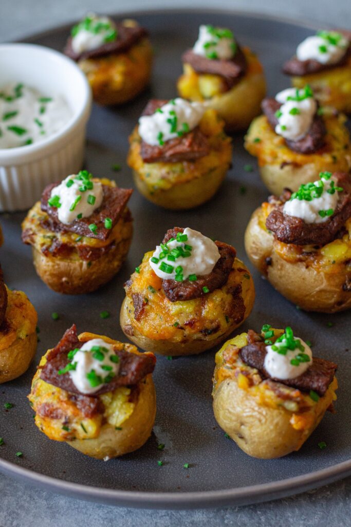 Plate of vegan steak ‘n’ potato bites served with a small bowl of garlic horseradish dipping sauce, garnished with fresh chives.