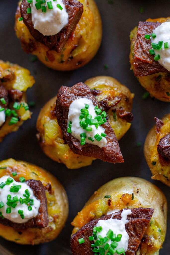 Plate of vegan steak ‘n’ potato bites served with a small bowl of garlic horseradish dipping sauce, garnished with fresh chives.