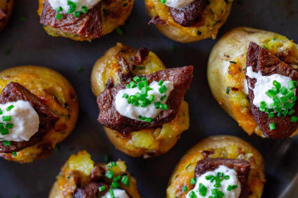 Plate of vegan steak ‘n’ potato bites served with a small bowl of garlic horseradish dipping sauce, garnished with fresh chives.