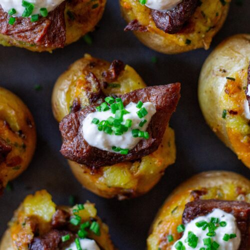 Plate of vegan steak ‘n’ potato bites served with a small bowl of garlic horseradish dipping sauce, garnished with fresh chives.