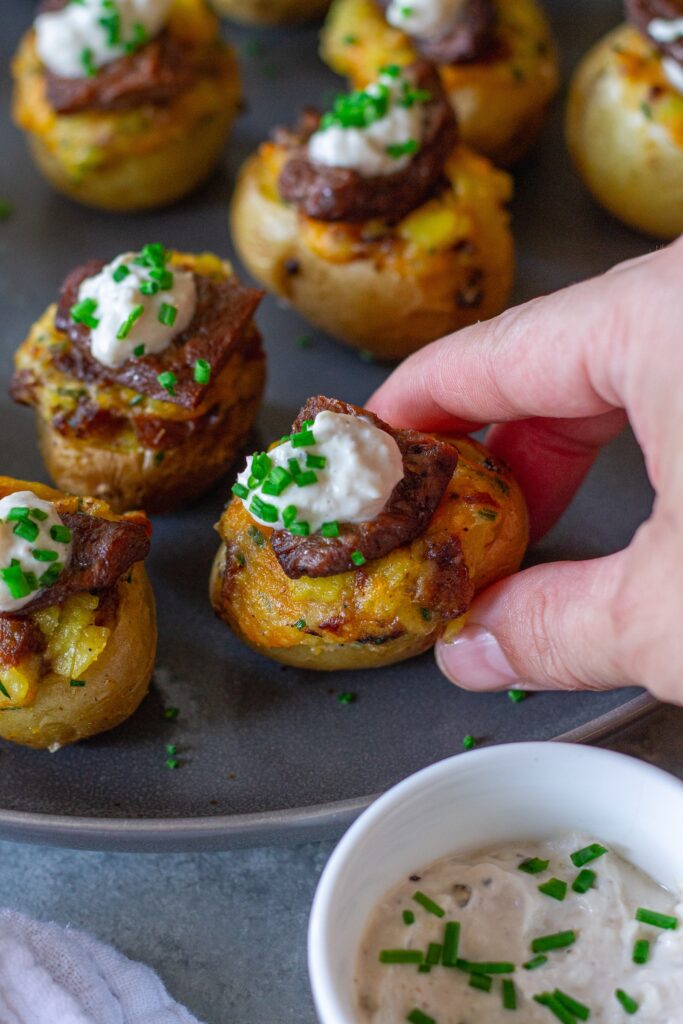 Plate of vegan steak ‘n’ potato bites served with a small bowl of garlic horseradish dipping sauce, garnished with fresh chives.