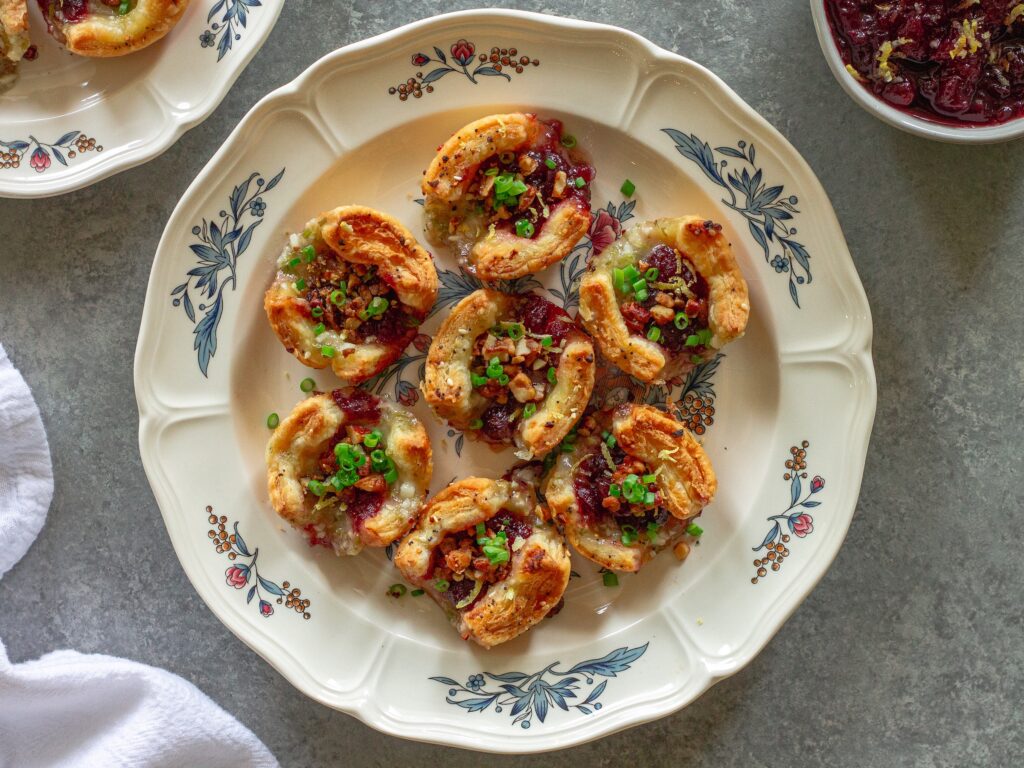 Golden brown Vegan Cranberry Cream Cheese Bites garnished with green onion, candied walnuts, and lemon zest, served on a festive platter.
