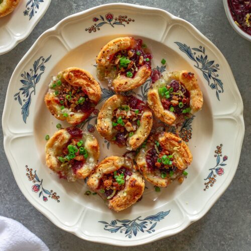 Golden brown Vegan Cranberry Cream Cheese Bites garnished with green onion, candied walnuts, and lemon zest, served on a festive platter.