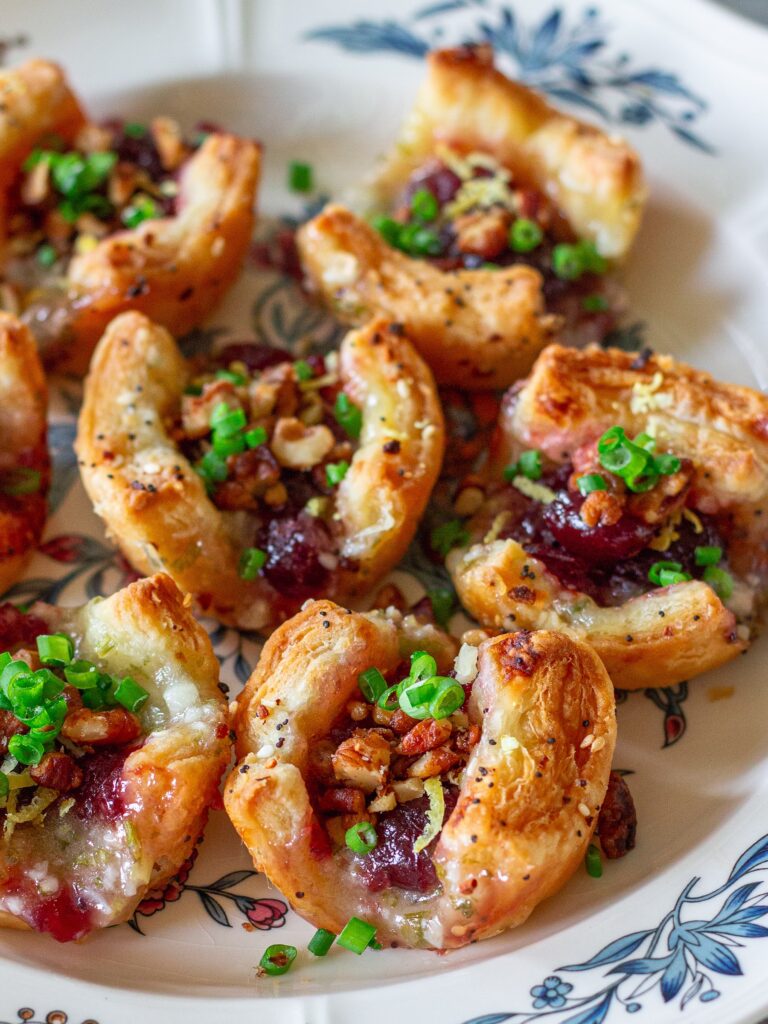 Golden brown Vegan Cranberry Cream Cheese Bites garnished with green onion, candied walnuts, and lemon zest, served on a festive platter.