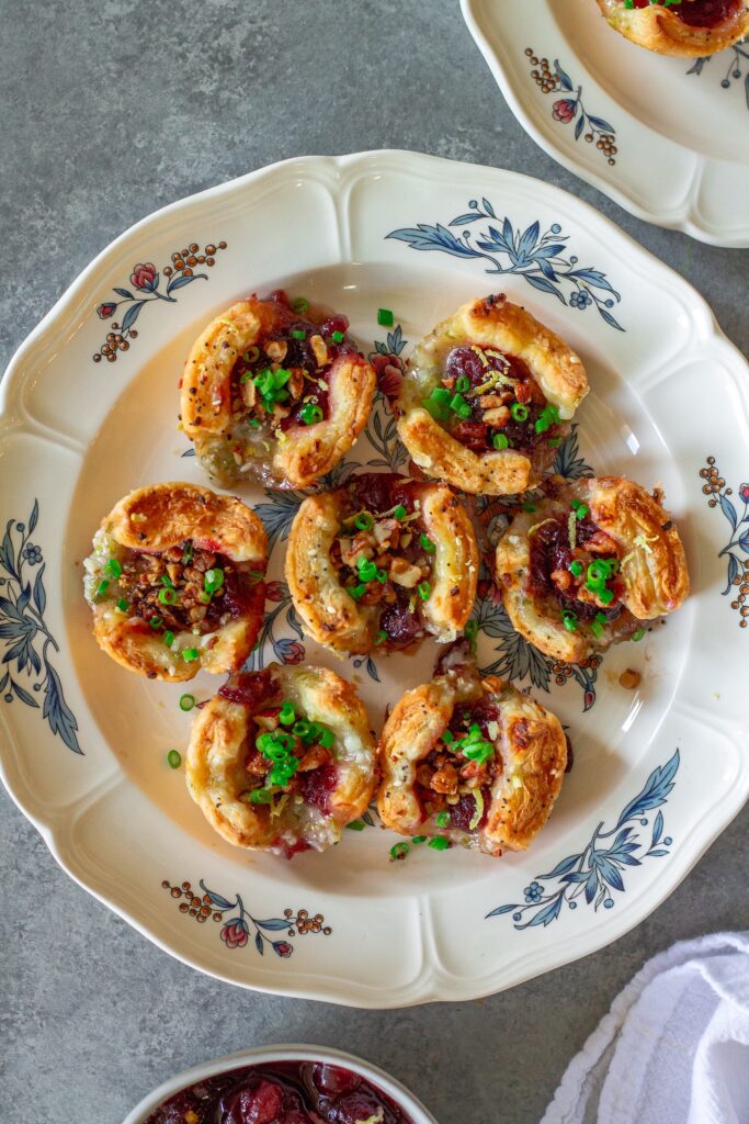 Golden brown Vegan Cranberry Cream Cheese Bites garnished with green onion, candied walnuts, and lemon zest, served on a festive platter.