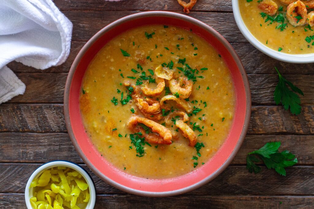 Vegan pepperoncini soup in a bowl, topped with crispy fried pepperoncini rings and fresh minced parsley for garnish.