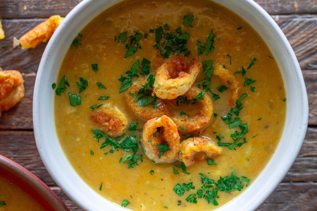 Vegan pepperoncini soup in a bowl, topped with crispy fried pepperoncini rings and fresh minced parsley for garnish.